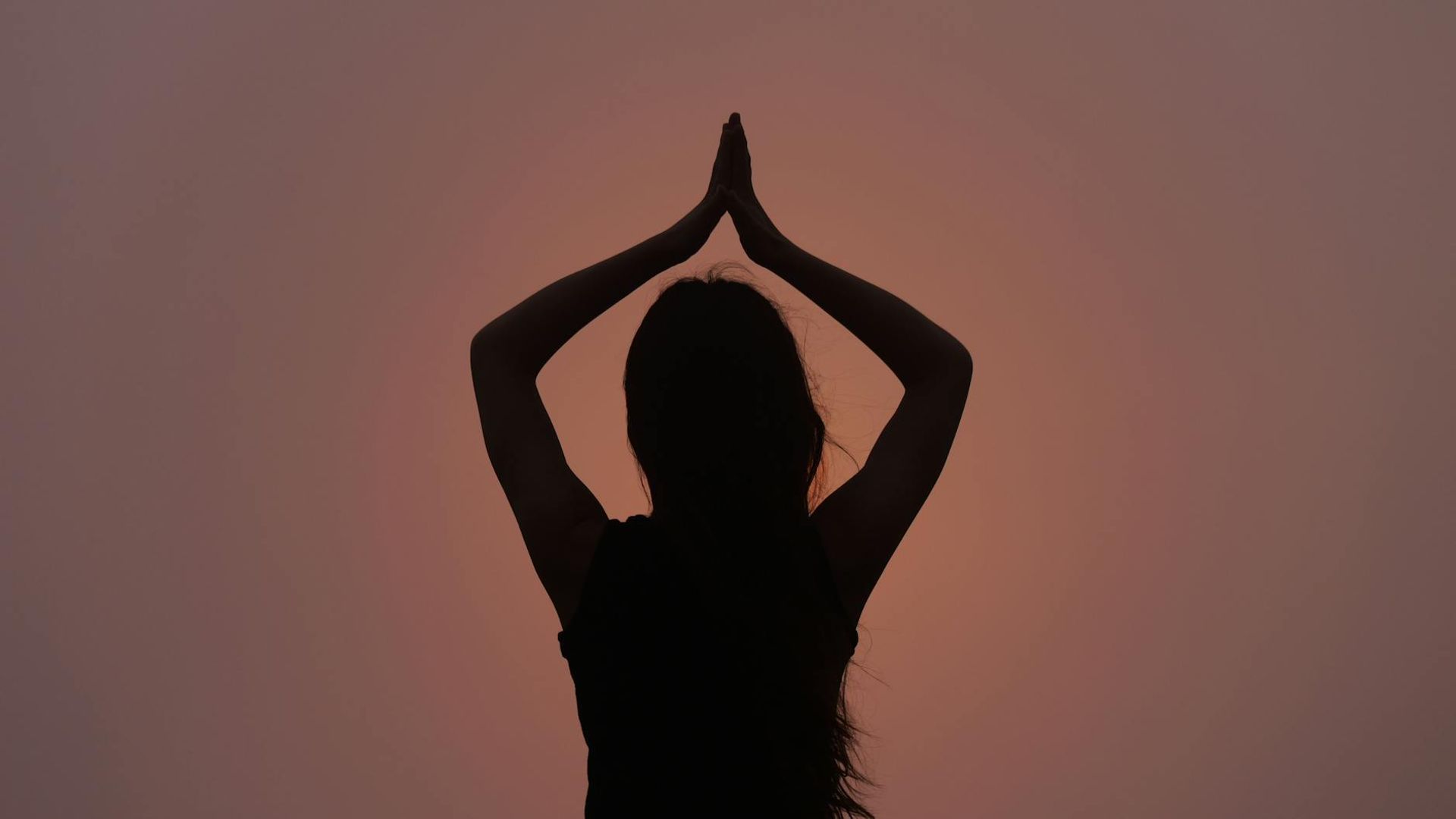 Woman practicing yoga silhouette against a dark background with ruby light.